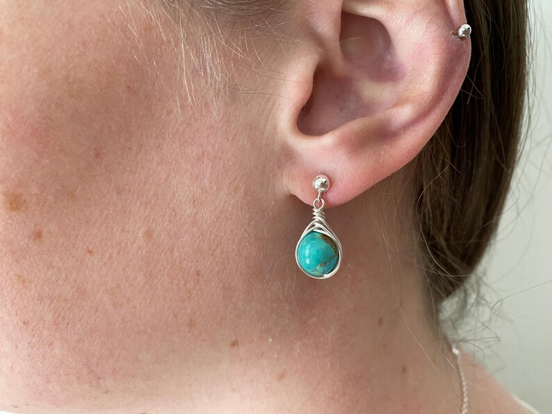 May include: A pair of silver earrings with turquoise stones. The earrings are teardrop shaped and have a wire wrapped design.