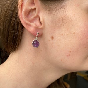 May include: A pair of silver earrings with a purple amethyst stone. The earrings are simple and elegant, perfect for everyday wear.