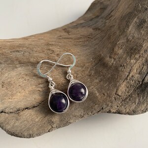 May include: A pair of silver wire wrapped earrings with dark purple amethyst stones.