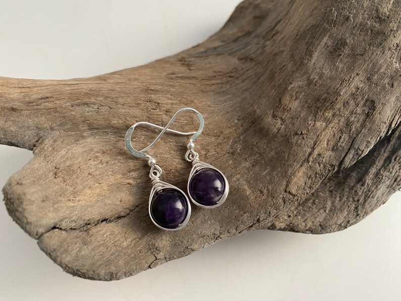 May include: A pair of silver wire wrapped earrings with dark purple amethyst stones.