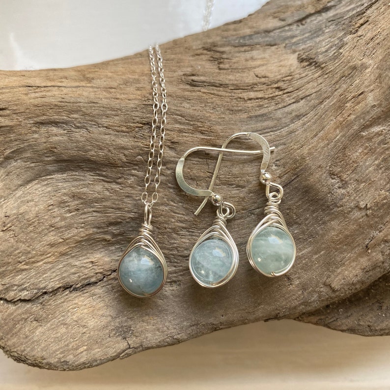 K&ouml;nnte beinhalten: Ein silbernes Halsketten- und Ohrring-Set mit Aquamarin-Steinen. Die Steine sind in Silberdraht gewickelt und haben eine Tropfenform.