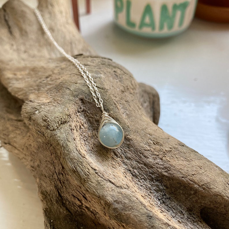 K&ouml;nnte beinhalten: Eine silberne Kettenkette mit einem Anh&auml;nger aus hellblauem Aquamarin, der in Silberdraht gewickelt ist.