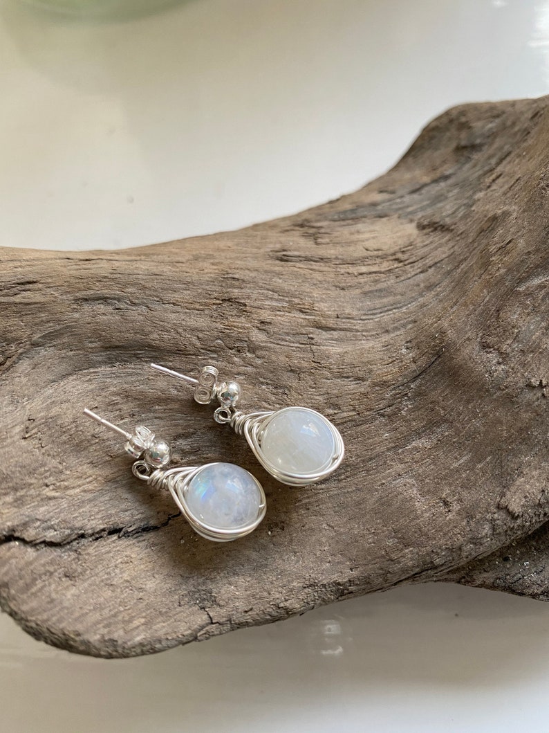 May include: A pair of silver wire wrapped earrings with round moonstone gemstones.