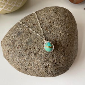 May include: A silver chain necklace with a turquoise gemstone pendant. The pendant is wrapped in silver wire and has a teardrop shape.