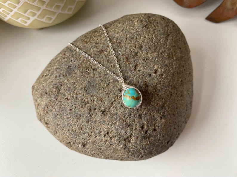 May include: A silver chain necklace with a turquoise gemstone pendant. The pendant is wrapped in silver wire and has a teardrop shape.