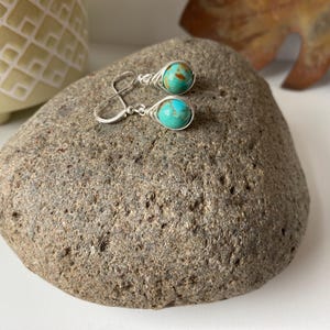 May include: A pair of silver earrings with turquoise stones. The stones are a mottled blue and green color.