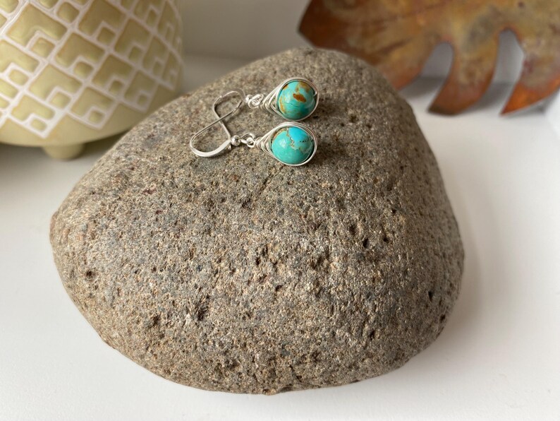 May include: A pair of silver earrings with turquoise stones. The stones are a mottled blue and green color.