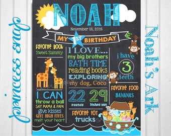 May include: A chalkboard-style first birthday sign for a boy named Noah. The sign features a blue and orange colour scheme with a giraffe, monkey, and ark theme. It includes details like favourite book, favourite food, and weight and height. The sign says "Noah's Ark" at the bottom.