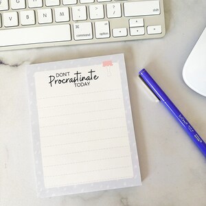 May include: A white notepad with a gray background and a pink drawing of a woman's legs. The notepad has a lined interior and the text "DON'T Procrastinate TODAY" printed on the front.