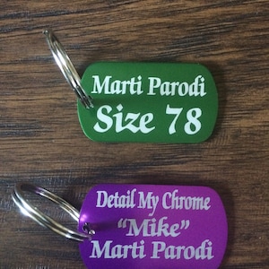 May include: Two metal keychains with engraved text. The top keychain is green and says "Marti Parodi Size 78". The bottom keychain is purple and says "Detail My Chrome "Mike" Marti Parodi".