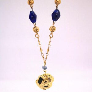 Puede incluir: Un collar de oro con un gran colgante de oro texturizado. El collar est&aacute; hecho de una cadena con peque&ntilde;as bolas de oro y cuentas de vidrio azul.