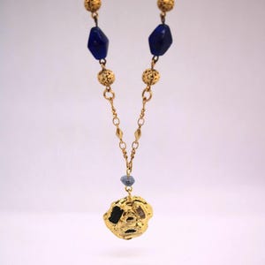 Puede incluir: Un collar de oro con un colgante de oro texturizado y cuentas de vidrio azules.