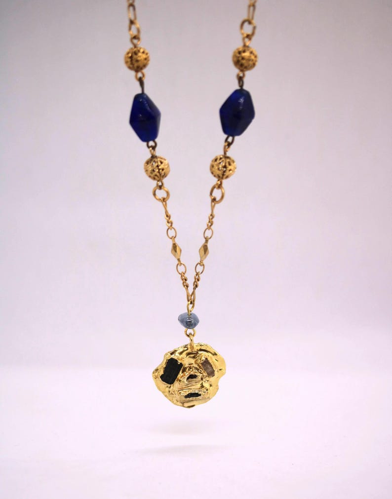 Puede incluir: Un collar de oro con un colgante de oro texturizado y cuentas de vidrio azules.