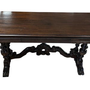 May include: Dark brown antique table with a rectangular top and ornate, carved legs. The table features a decorative apron with carved details and a rich, polished finish. The table's design is reminiscent of classic furniture styles.