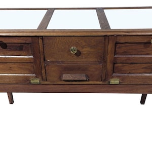May include: A vintage wooden display cabinet with a glass top and multiple drawers. The cabinet has a warm brown finish, brass hardware, and slender legs. The glass top is divided into three sections.