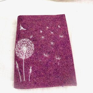 May include: A rectangular, deep purple felt case featuring a white dandelion design. The dandelion is depicted with a detailed seed head and delicate stems. A silver framed picture is in the background.