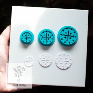 May include: A set of three turquoise and three white circular craft tools with a cross design. The tools are arranged on a white surface. The tools are different sizes. The smallest tool is 1 inch in diameter, the medium tool is 1.5 inches, and the largest tool is 2 inches.