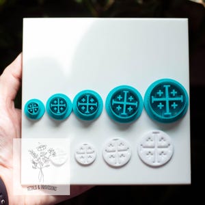 May include: A collection of teal and white cookie cutters in various sizes, featuring a cross design. The cutters are arranged on a white surface, with a small illustration and text "Petals & Provisions" in the corner.