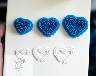 May include: A collection of heart-shaped cookie cutters in blue and white. The blue cutters are in three sizes, while the white cutters are in two sizes. The cutters have a pencil design. The image also includes the text "PETALS & PROVISIONS".