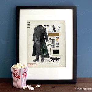 May include: Framed print with illustrations from "The Matrix", including a long black coat, sunglasses, and a black cat. The year "1999" is displayed. A popcorn container with popcorn is in the foreground. The print is in a black frame.