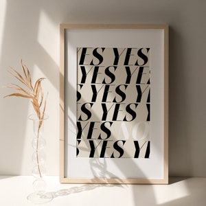 May include: A framed print with the word "YES" repeated multiple times in a black and white design. The print is on a beige background and is framed in a light wood frame.