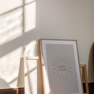 Puede incluir: Una impresi&oacute;n enmarcada con un fondo beige y texto negro que dice "ENERGY GIVERS" en un c&iacute;rculo con flechas que apuntan a palabras como "meditaci&oacute;n", "lectura", "baile" y "naturaleza". La impresi&oacute;n est&aacute; en un marco de madera claro y se apoya contra una pared blanca.