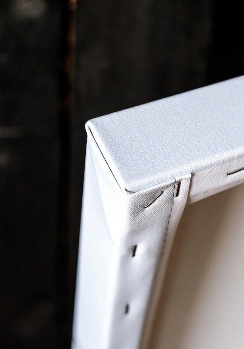 May include: Close-up of the corner of a white canvas stretched over a wooden frame. The canvas is secured with staples.