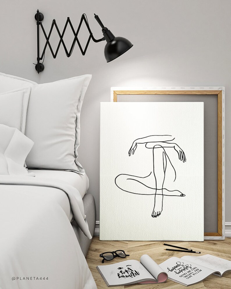 May include: A black and white line drawing of a person sitting with their legs crossed. The drawing is on a white canvas with a wooden frame. The canvas is leaning against a white wall.