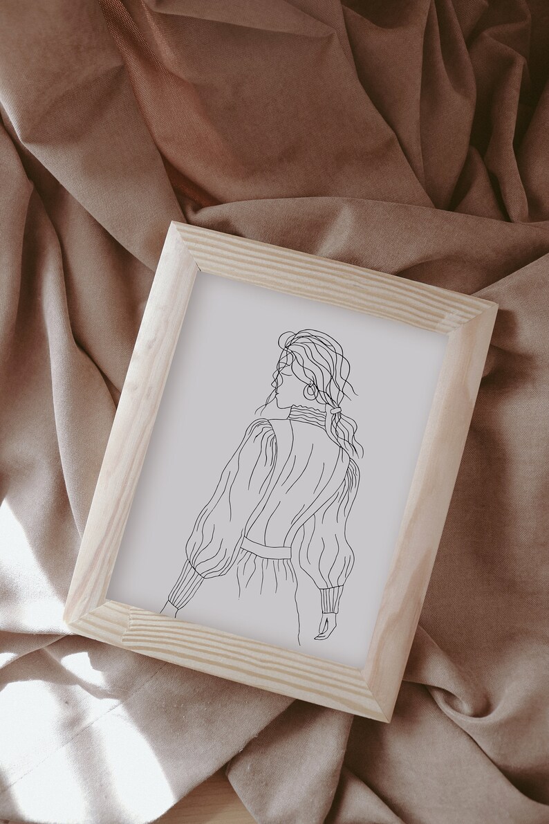 K&ouml;nnte beinhalten: Eine gerahmte Linienzeichnung einer Person mit langen Haaren, die ein lang&auml;rmliges Kleid tr&auml;gt. Die Zeichnung ist in Schwarzwei&szlig; und auf wei&szlig;em Hintergrund.