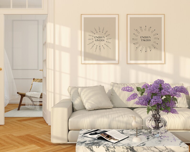 Puede incluir: Dos impresiones enmarcadas con el texto "Energy Givers" y "Energy Takers" en una sala de estar con un sof&aacute; blanco, una mesa de caf&eacute; y un jarr&oacute;n de flores moradas.