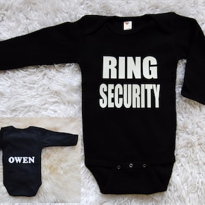 May include: Black long-sleeve bodysuit with white text that reads "RING SECURITY" on the front and "OWEN" on the back.