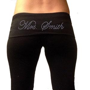 May include: Black yoga pants with a wide waistband featuring the text "Mrs. Smith" in white rhinestones.