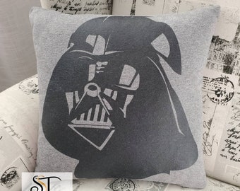 May include: A grey cushion featuring a black silhouette of Darth Vader's face. The cushion has the text "ST SEAMS SEW THREADY" printed on the bottom.