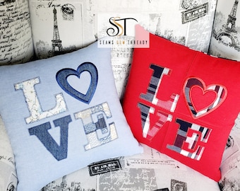 May include: Two decorative throw pillows with the word "LOVE" embroidered in colourful patchwork fabric. The pillows are blue and red with white accents.