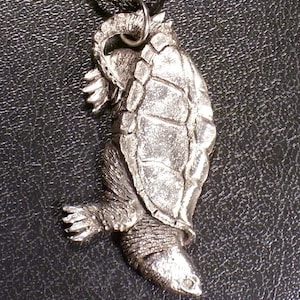 May include: A silver pendant necklace featuring a detailed sculpture of a turtle with its head tucked inside its shell.