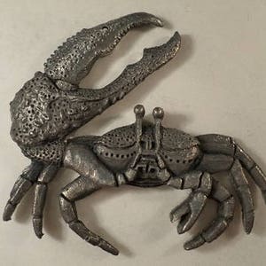 May include: A silver-colored metal sculpture of a crab with detailed textured claws and body.