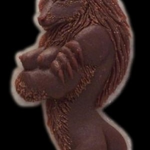 Pode incluir: Uma figura de lobisomem marrom com uma textura de pelo detalhada. O lobisomem está em pé sobre suas patas traseiras com os braços cruzados na frente do peito.