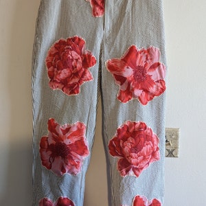 May include: White pants with thin black stripes and red and pink floral appliques.