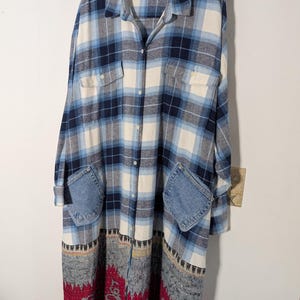 May include: A long-sleeved button-down shirt dress featuring a blue, white, and navy plaid pattern on the upper portion, two chest pockets, two denim patch pockets at the hips, and a contrasting red and grey patterned fabric at the hem.
