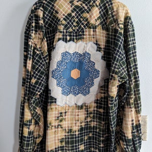 May include: A black and tan plaid flannel shirt with a large, white, blue, and orange patchwork flower design on the back.