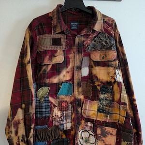 May include: A red and black plaid flannel shirt with various fabric patches sewn on. The shirt has been bleached and distressed, giving it a vintage look.
