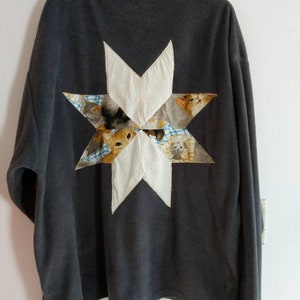 May include: A dark gray fleece jacket with a large white star patch on the back. The star is made of fabric with a cat print.