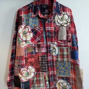 May include: A red and black plaid flannel shirt with patchwork details and embroidered flowers. The shirt has a button-up front and long sleeves.