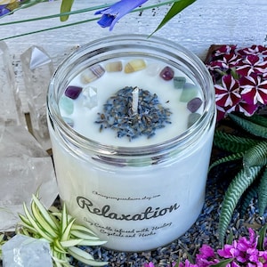 May include: A white soy candle with a clear glass jar and a label that reads "Relaxation Soy Candle infused with Healing Crystals and Herbs". The candle is decorated with lavender buds and small crystals.