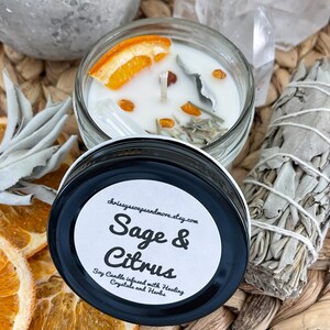 May include: A white soy candle in a glass jar with a black lid. The candle is infused with sage, citrus, crystals, and herbs. The jar has a white label with the text "Sage & Citrus" and "Soy Candle infused with Healing Crystals and Herbs".