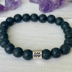 Peut inclure: Bracelet en perles de roche volcanique noire avec un charme argent&eacute; repr&eacute;sentant le signe du zodiaque Verseau.