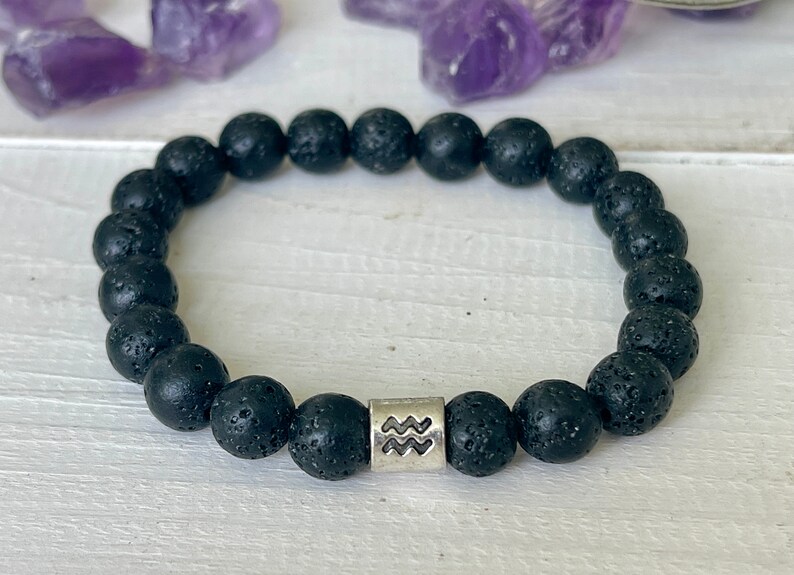 Peut inclure: Bracelet en perles de roche volcanique noire avec un charme argent&eacute; repr&eacute;sentant le signe du zodiaque Verseau.