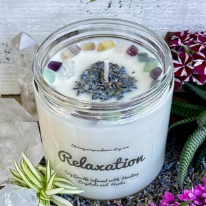 May include: A white soy candle in a clear glass jar with a label that reads "Relaxation Soy Candle infused with Healing Crystals and Herbs". The candle is surrounded by lavender flowers, crystals, and greenery.