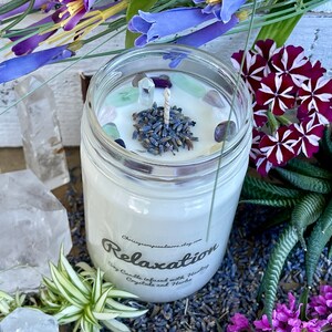 May include: A white soy candle in a clear glass jar with a lavender and crystal top. The candle is labeled "Relaxation Soy Candle Infused with Healing Crystals and Herbs".