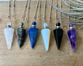Op de afbeelding: Zeven kristallen kettingen met zilveren kettingen. De hangers zijn in de vorm van een piramide en zijn gemaakt van helder kwarts, groen en rood jaspis, blauw lapis lazuli, witte opaal, zwarte obsidiaan en amethist.